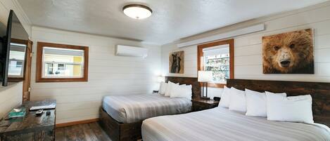 A bedroom with two beds, a wooden dresser, a mirror, and a bear painting on the wall.