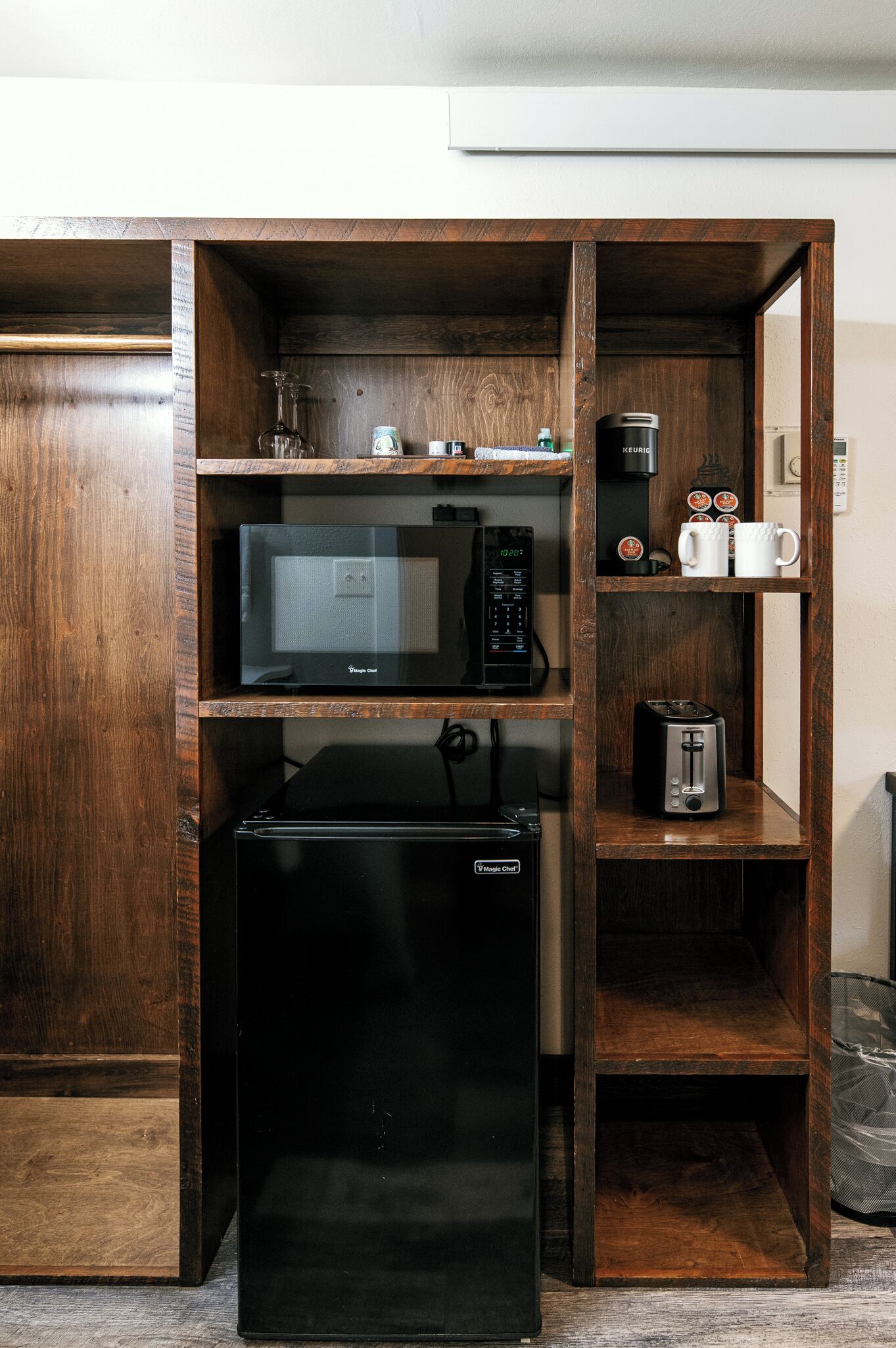 A compact kitchen with a microwave, toaster, and coffee maker on wooden shelves.