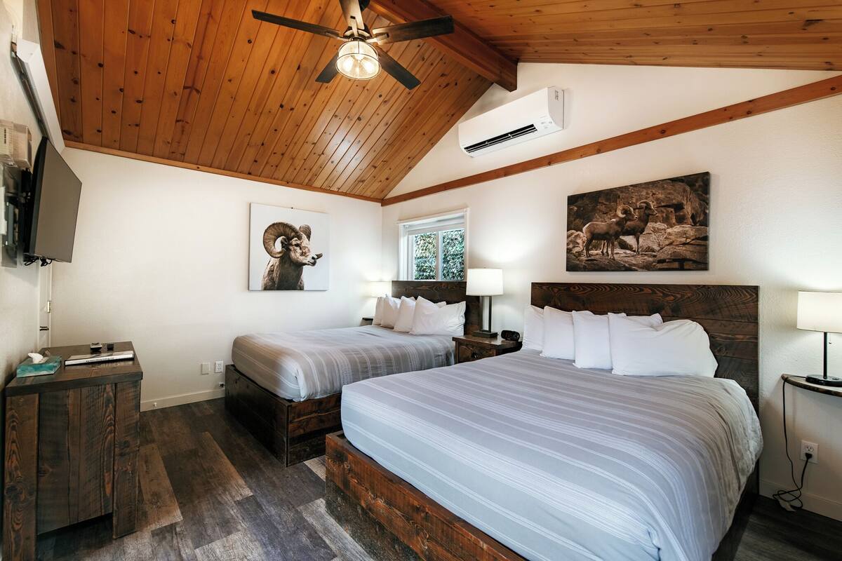 A bedroom with two beds, wooden ceiling beams, a mounted TV, and artwork on the walls.