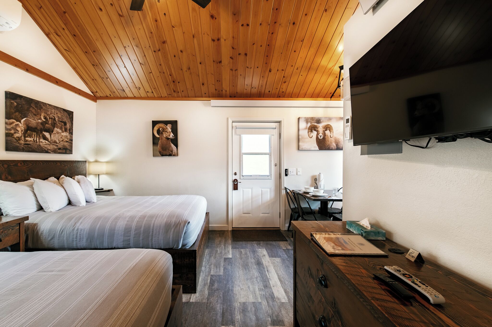 Ein Hotelzimmer mit zwei Betten, einer Holzbalkendecke, einem Fernseher und einer Tür.