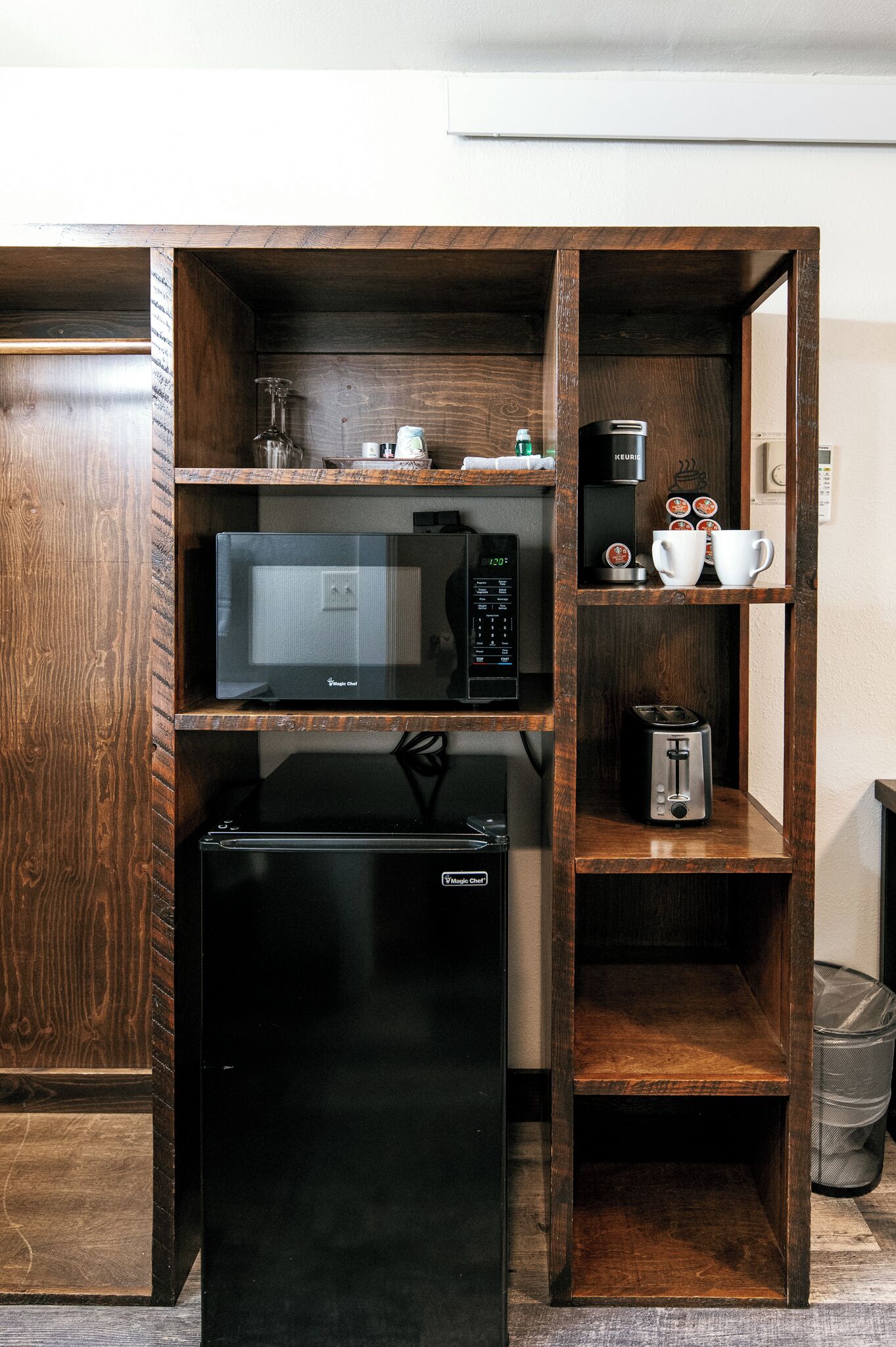 A compact kitchenette with a microwave, toaster, and coffee maker on wooden shelves.