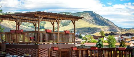 A wooden pergola with potted plants, a gravel ground, and a mountainous backdrop.