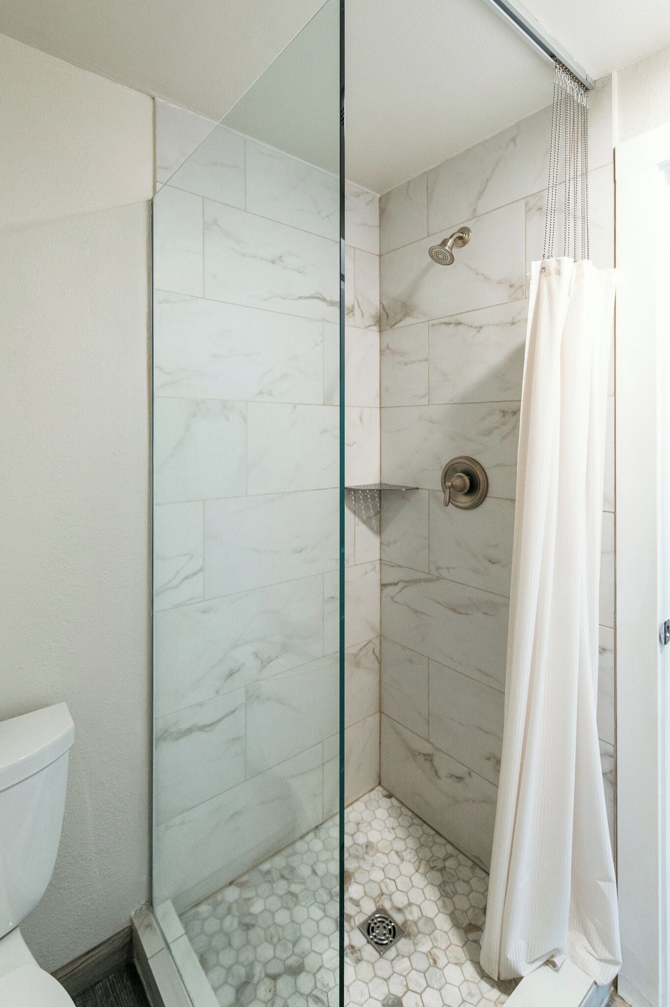 Une douche avec une porte en verre, un pommeau de douche et un rideau.