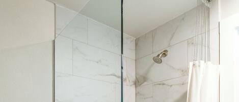 Une douche avec une porte en verre, un pommeau de douche et un rideau.