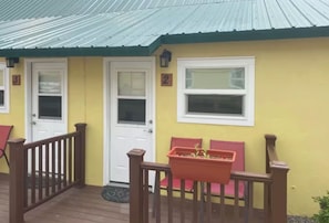 A yellow building with a metal roof, two white doors, and a window.
