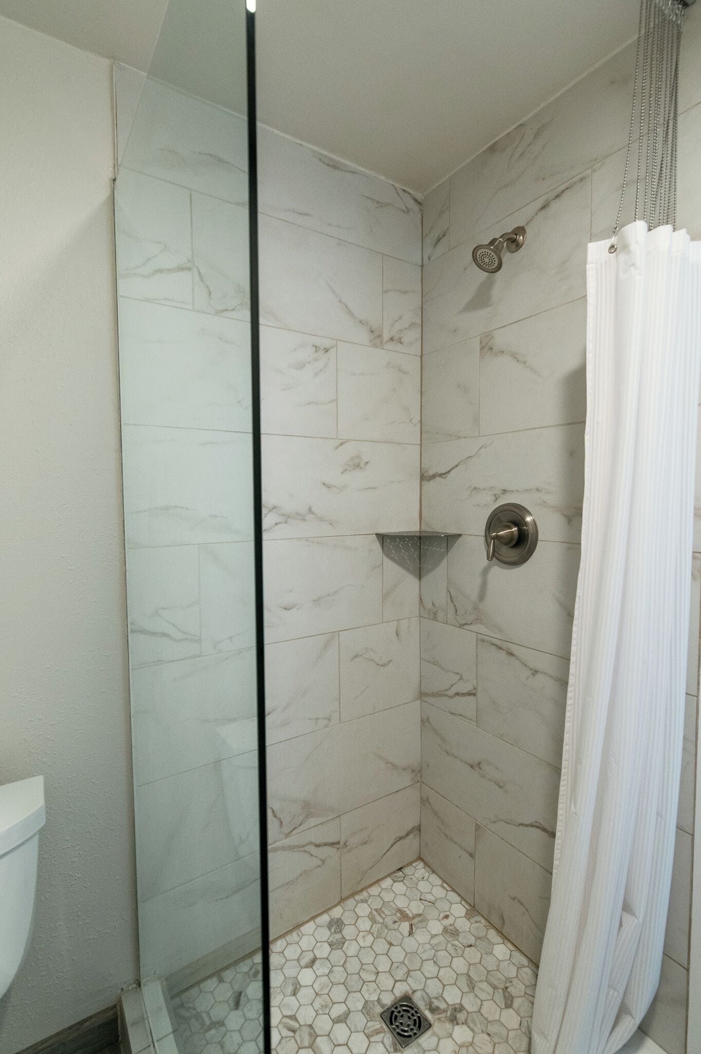 A shower with a glass door, a showerhead, and a tiled floor.