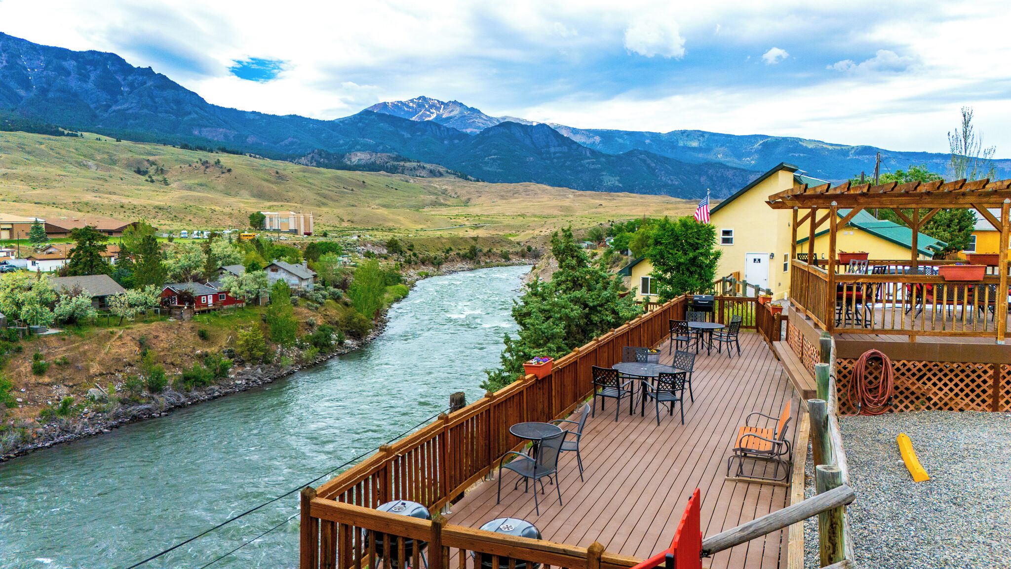 A riverside deck with outdoor seating, overlooking a river and mountains.