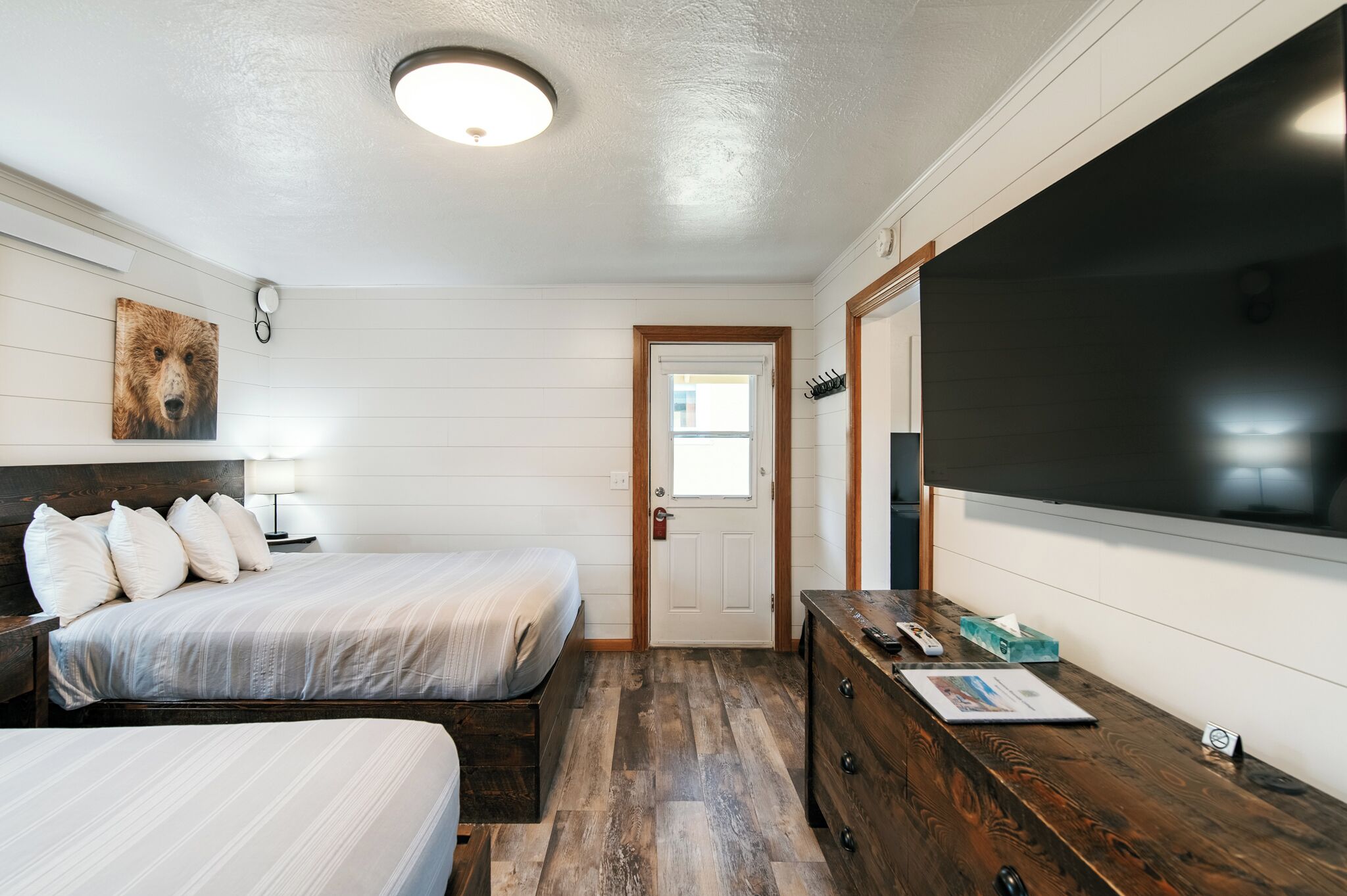 Un dormitorio con cama, mesita de noche, cómoda y un televisor grande.