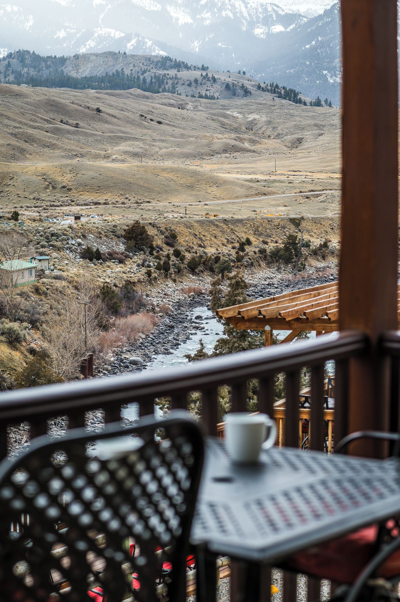 A view from a balcony overlooking a river, mountains, and a small building.