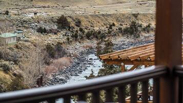 A view from a balcony overlooking a river, mountains, and a small building.