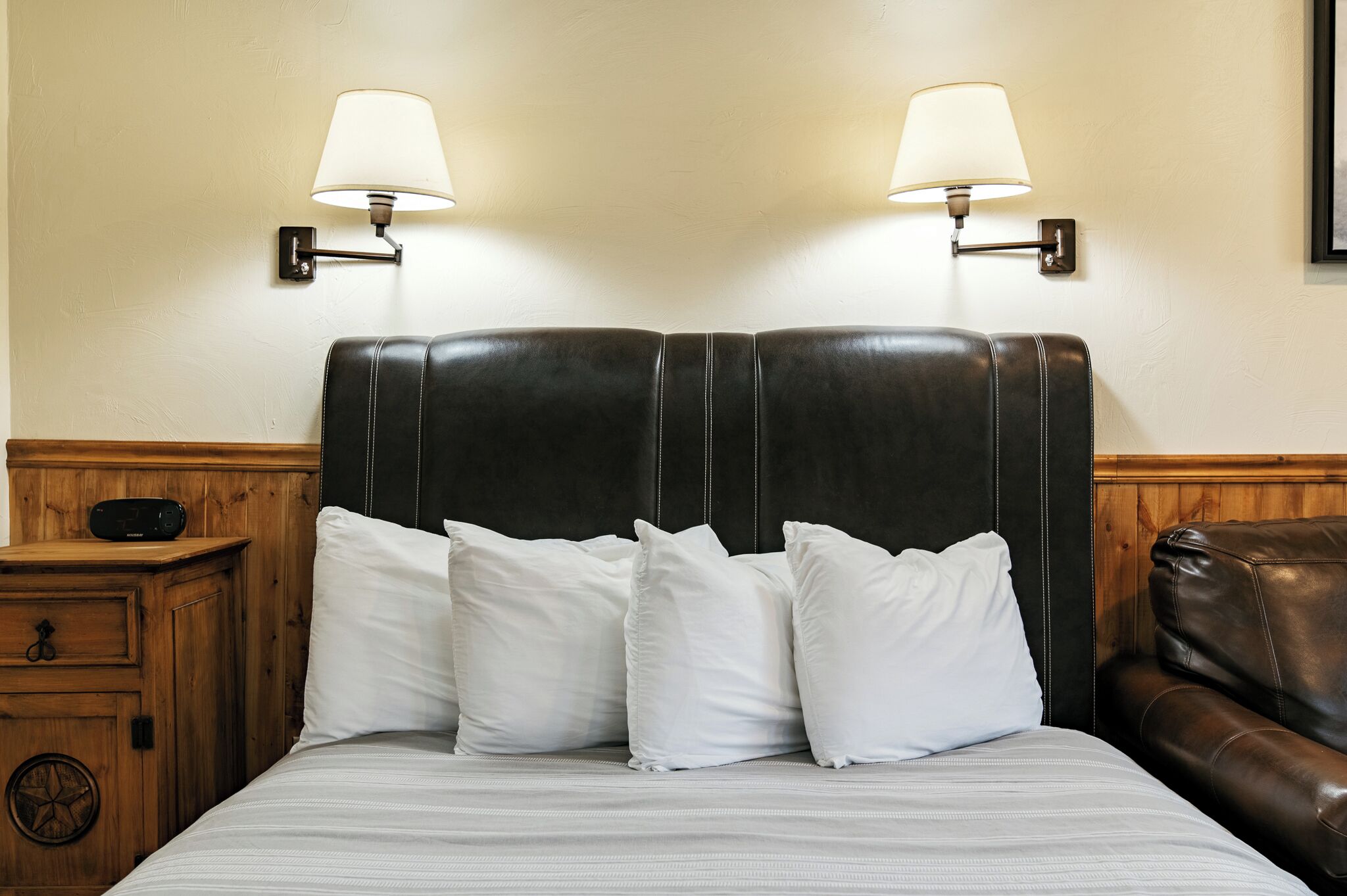 A bed with white bedding, a dark headboard, and two wall-mounted lamps.