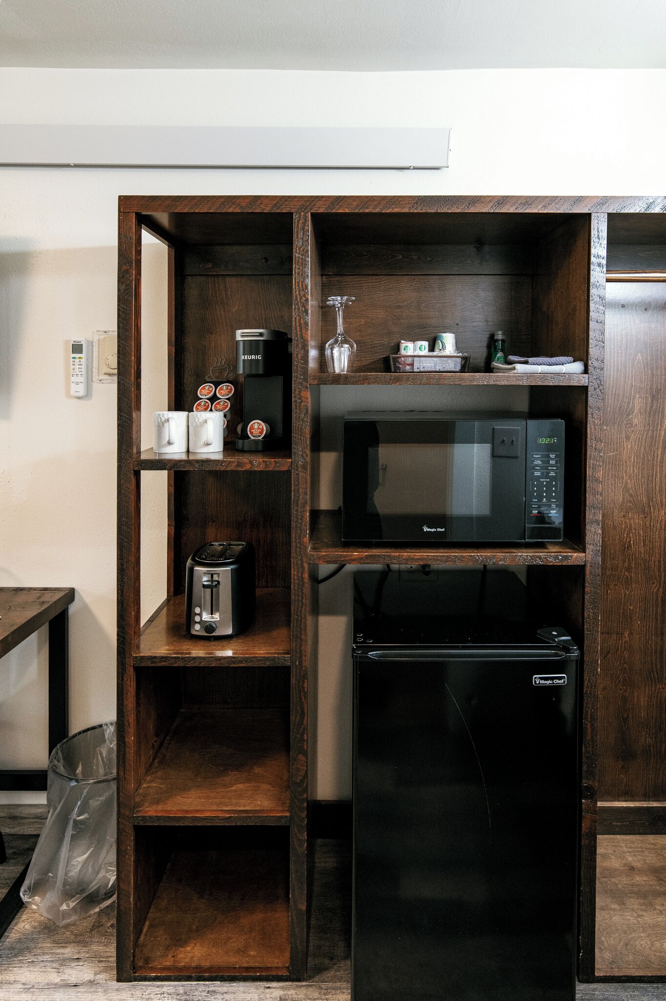 A kitchenette with a microwave, toaster, and coffee maker on wooden shelves.