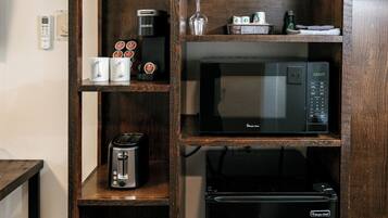 A kitchenette with a microwave, toaster, and coffee maker on wooden shelves.