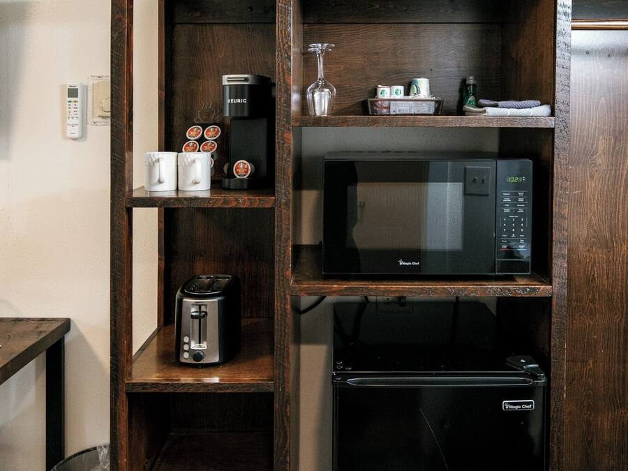 A kitchenette with a microwave, toaster, and coffee maker on wooden shelves.