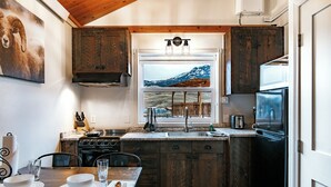 Una cocina pequeña con armarios de madera, estufa, lavabo y ventana con vista a la montaña.
