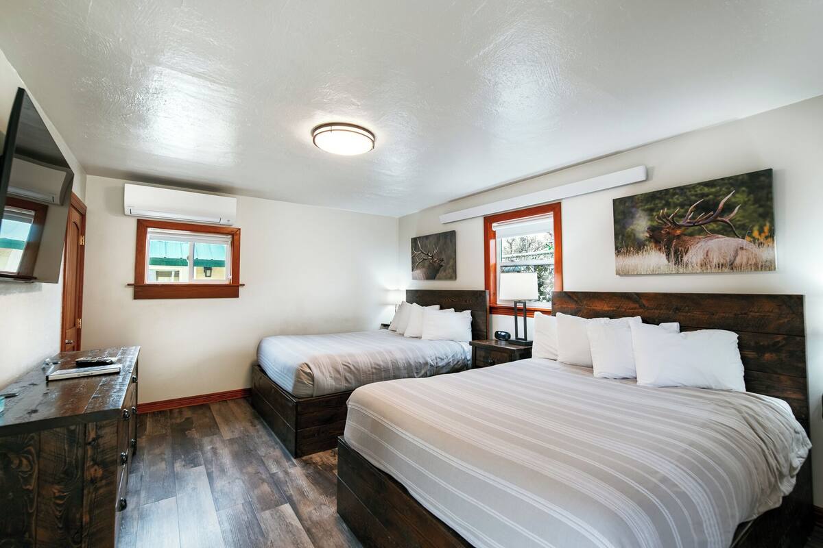 A bedroom with two beds, a wooden dresser, a TV, and artwork on the walls.