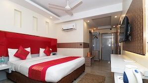 A hotel room with a large bed, a flat-screen TV, a coffee machine, and a bathroom with a shower and toilet. - Hotel Krishna Plaza (New Delhi)