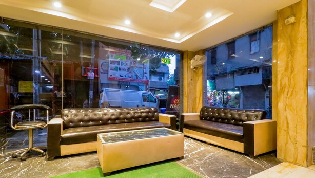 A lobby with two leather sofas, a glass coffee table, and a green rug. - Hotel Krishna Plaza (New Delhi)