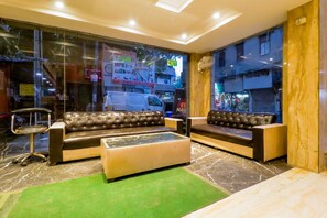 A lobby with two leather sofas, a glass coffee table, and a green rug. - Hotel Krishna Plaza (New Delhi)