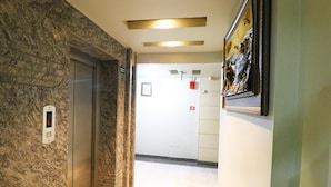 A hallway with a marble floor, an elevator, and a framed artwork on the wall. - Hotel Krishna Plaza (New Delhi)