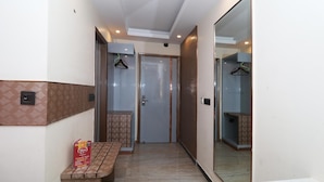 A hallway with a bench, a door, and a mirror reflecting the room. - Hotel Krishna Plaza (New Delhi)