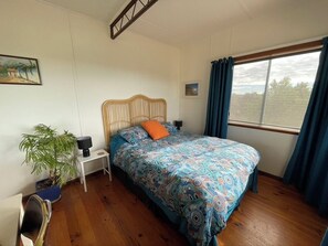 A bedroom with a bed, a bedside table, a lamp, a potted plant, and a window with curtains.