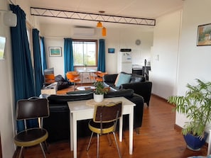 A compact living space with a dining area, a sofa, a small kitchen, and a potted plant. - Cosy retro weekender with far-reaching views (Goolwa Beach)