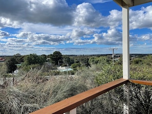 Un balcon donnant sur un paysage rural, avec des arbres et un bâtiment situé au loin.