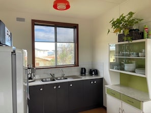 A kitchen with a window, a sink, a coffee maker, and a plant on the counter. - Cosy retro weekender with far-reaching views (Goolwa Beach)