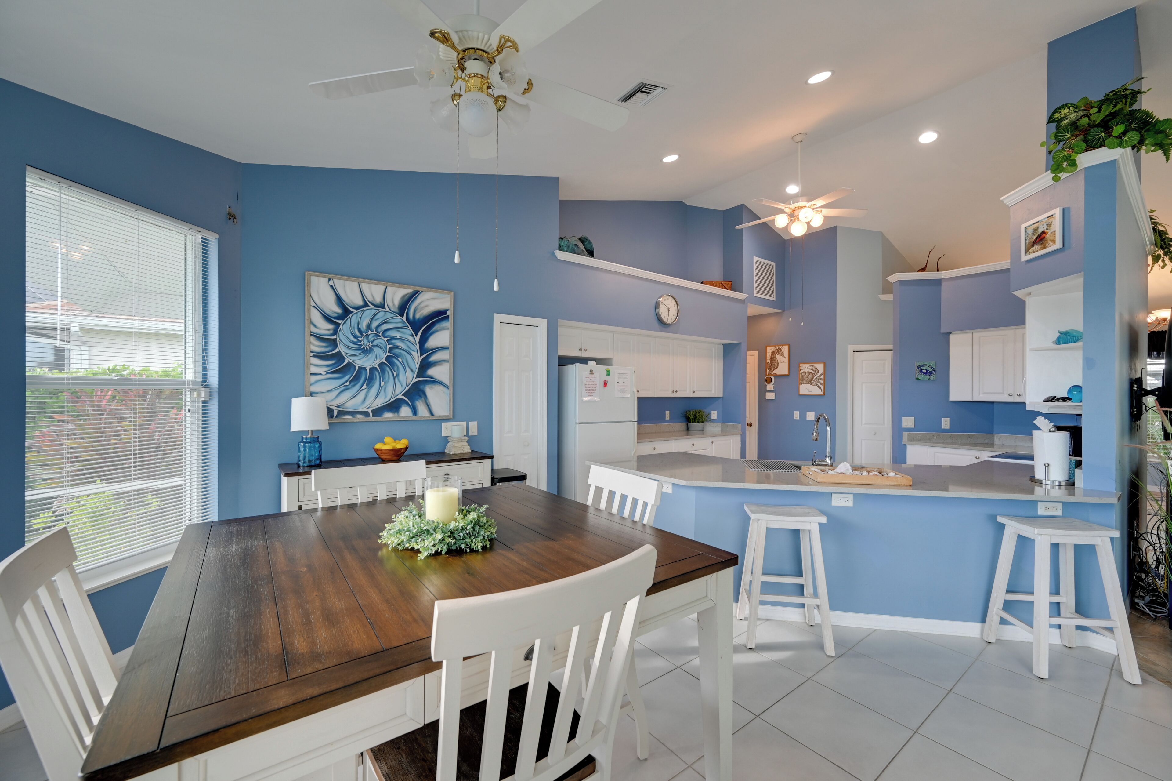 A modern kitchen with white cabinets, a central island, and a dining area with a wooden table and white chairs.