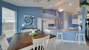 Una cocina moderna con armarios blancos, una isla central y un comedor con una mesa de madera y sillas blancas.