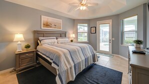 Un dormitorio con cama, mesita de noche, lámpara, ventilador de techo y ventanas.