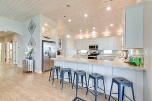 Una cocina moderna con armarios blancos, una isla grande con taburetes de bar, electrodomésticos de acero inoxidable e iluminación colgante.
