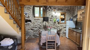 Une cuisine chaleureuse avec un mur en pierre, un escalier en bois et un coin repas agrémenté d’une nappe à carreaux.