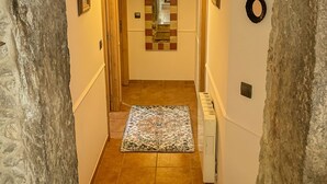 Un couloir étroit aux murs de pierre, orné d’un tapis à motifs et éclairé par un luminaire suspendu.