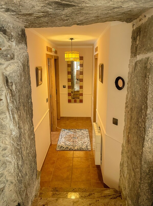 A narrow hallway with stone walls, a patterned rug, and a hanging light fixture.
