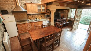 Une cuisine rustique avec des meubles de rangement en bois, un mur en pierre, une table à manger en bois et un four encastré.