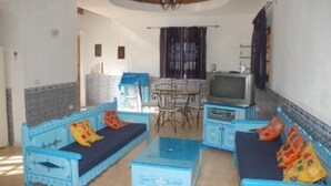 A living room with blue furniture, a TV, and a dining area. - House / Villa - Guizen djerba (djerba)