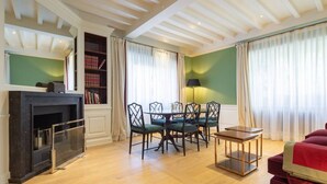 Ein Zimmer mit Kamin, einem Esstisch mit Stühlen, einem roten Sofa und einem Bücherregal.