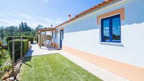 A modern house with a white exterior, a red-tiled roof, and a blue window. There is a patio area with a table and chairs, and a well-maintained lawn. - Digne Blue Villa, Pool, BBQ (Rogil, Aljezur)