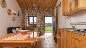 A kitchen with stone walls, wooden cabinets, a large table with a placemat, and a view through the open door. - Digne Blue Villa, Pool, BBQ (Rogil, Aljezur)