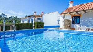 A swimming pool with clear blue water, surrounded by white buildings with red-tiled roofs and blue accents. - Digne Blue Villa, Pool, BBQ (Rogil, Aljezur)