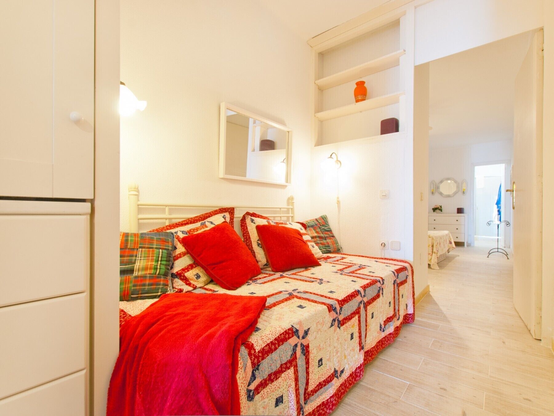 A bedroom with a bed, a mirror, a dresser, and a shelf with decorative items.