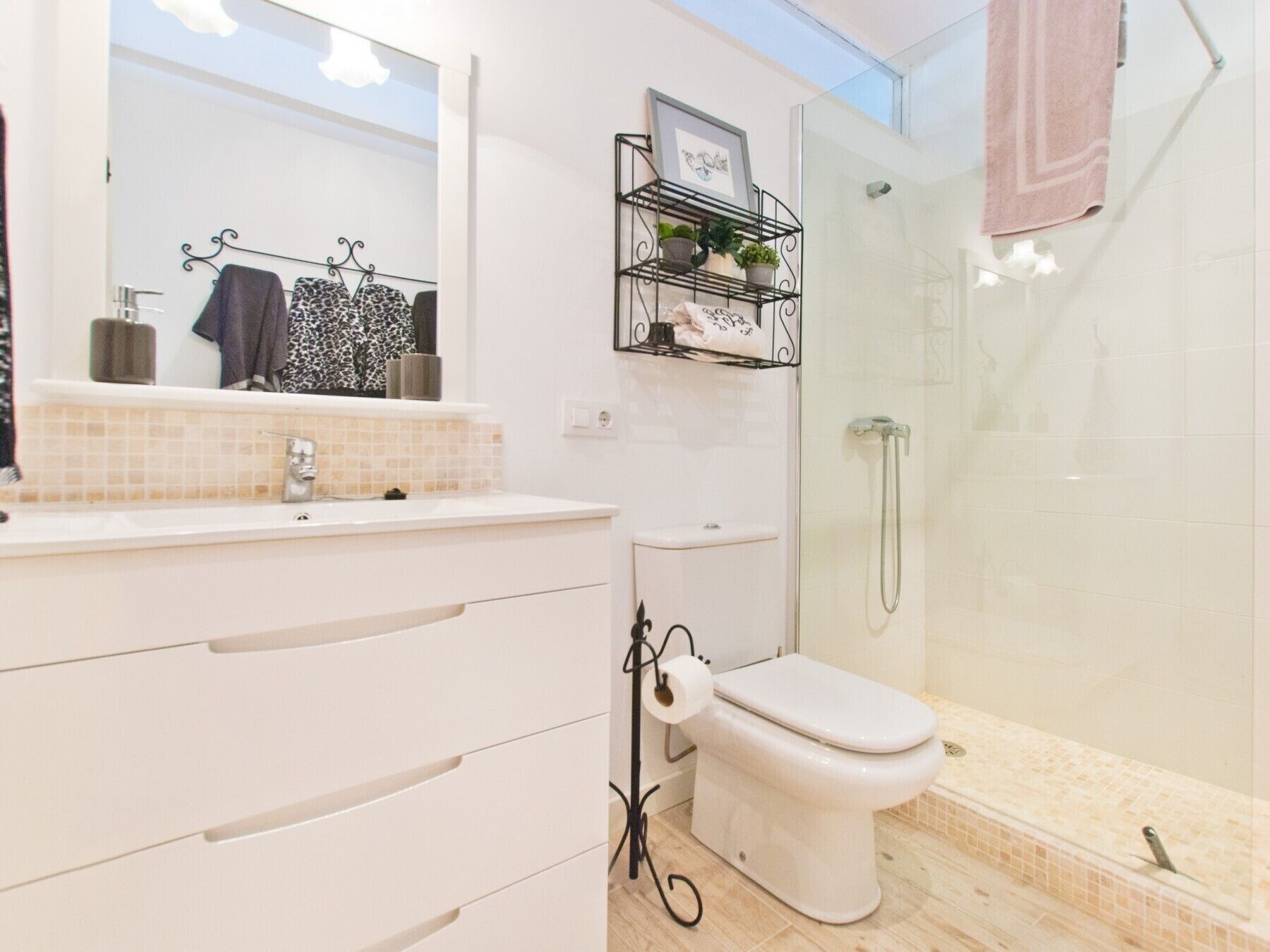 Ein modernes Badezimmer mit einem weißen Waschbecken, einer Toilette und einer Dusche. Ein Handtuchhalter mit einem pinken Handtuch und ein gerahmtes Bild über dem Waschbecken.