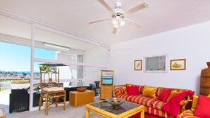 A spacious living area with a large window overlooking a beach, a ceiling fan, and a sofa with red cushions. - A. Oiza Sand Castle 24, Apt. 24 Edificio Canopus (Alcúdia)
