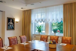 Un salón de conferencias con una larga mesa, sillas, una planta en maceta y una ventana con cortinas.