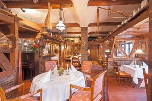 A rustic dining area with wooden beams, brick walls, and a round table set for dining. - Hotel Restaurant Grotehof (Minden)