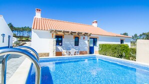 A swimming pool with a clear blue water, a white building with a red-tiled roof, and a small patio area with a table and chairs. - Digne Orange Villa, Pool, BBQ (Rogil, Aljezur)