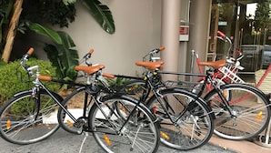 Drei Fahrräder sind in einer Reihe geparkt, mit einem Gebäude und Grünflächen im Hintergrund.