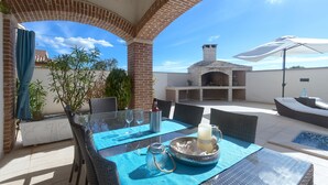 Une terrasse extérieure agrémentée d’une arche en briques, d’une table en verre et d’un espace barbecue.